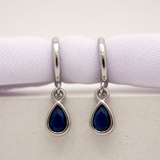 Teardrop-shaped blue gemstone earrings with silver hooks on a white background