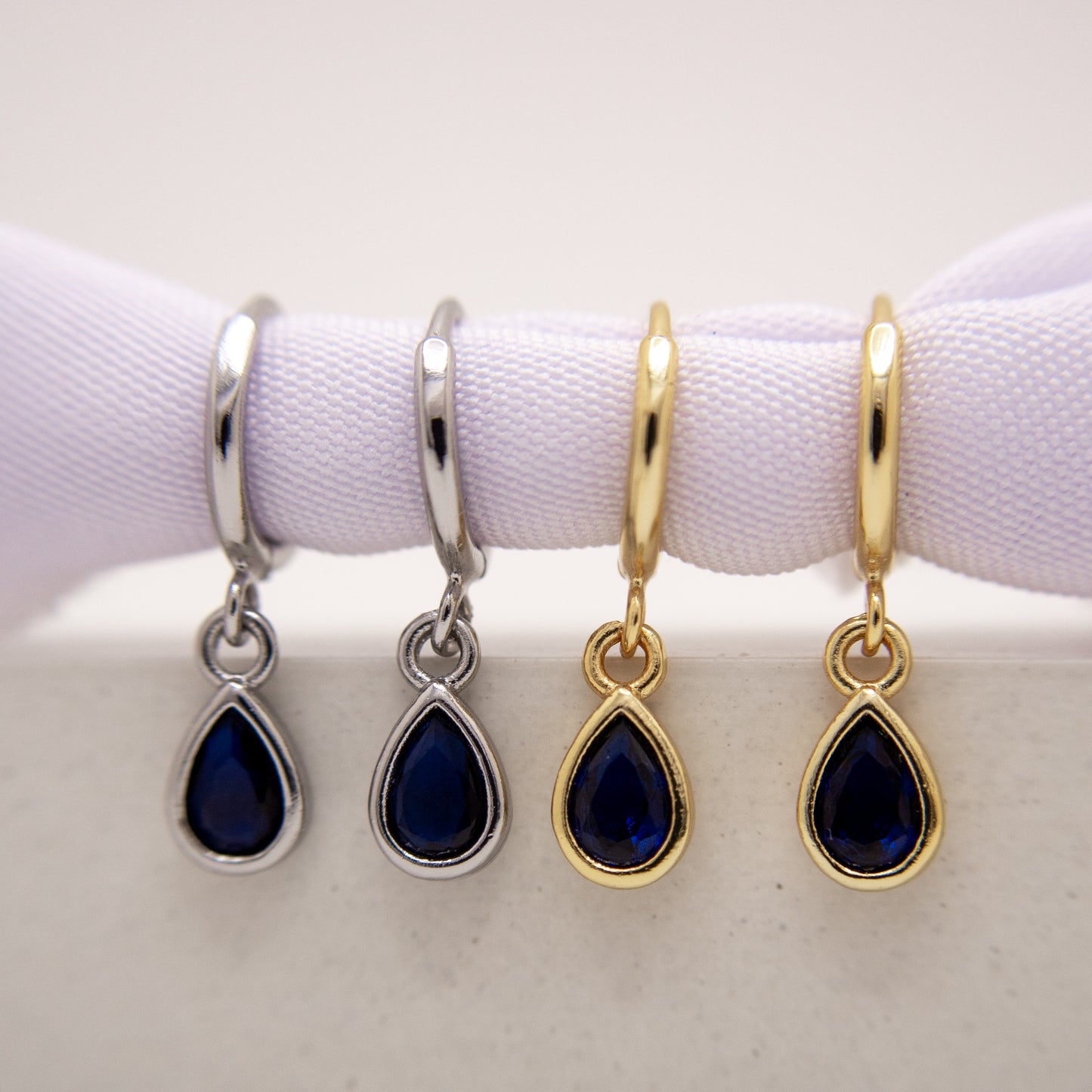 Four pairs of earrings with teardrop-shaped blue stones on a white background