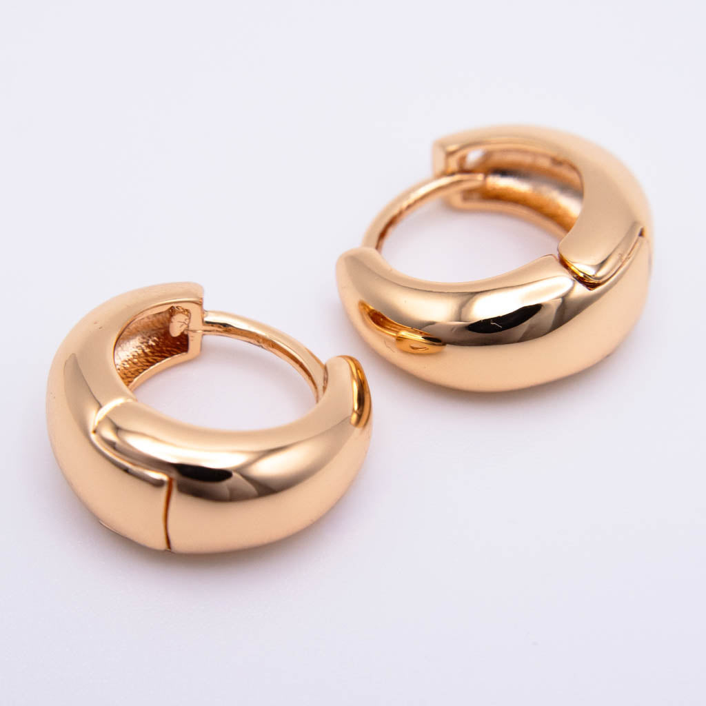 A pair of chunky, polished gold huggie hoop earrings on a clean white background.