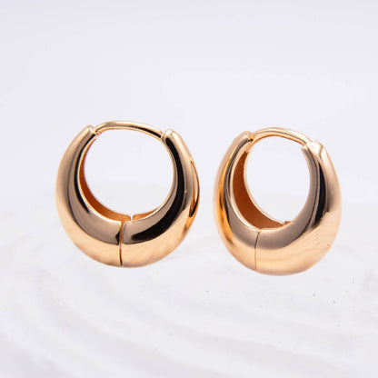 A pair of polished rose gold hoop earrings with a unique curved, teardrop-like shape and a central seam, displayed on a clean white surface.