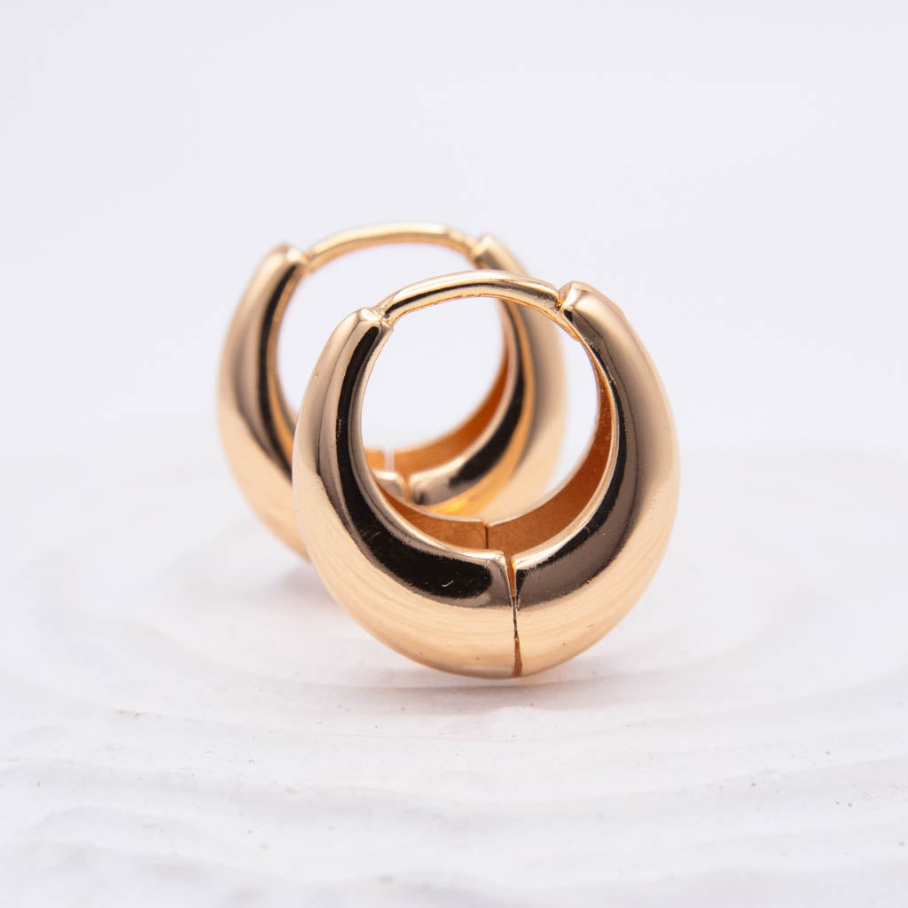 A pair of polished gold huggie hoop earrings on a white textured background.