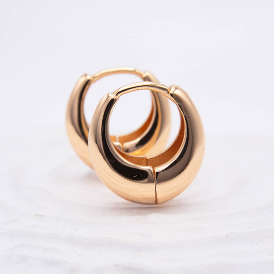 A pair of polished gold huggie hoop earrings on a white textured background.