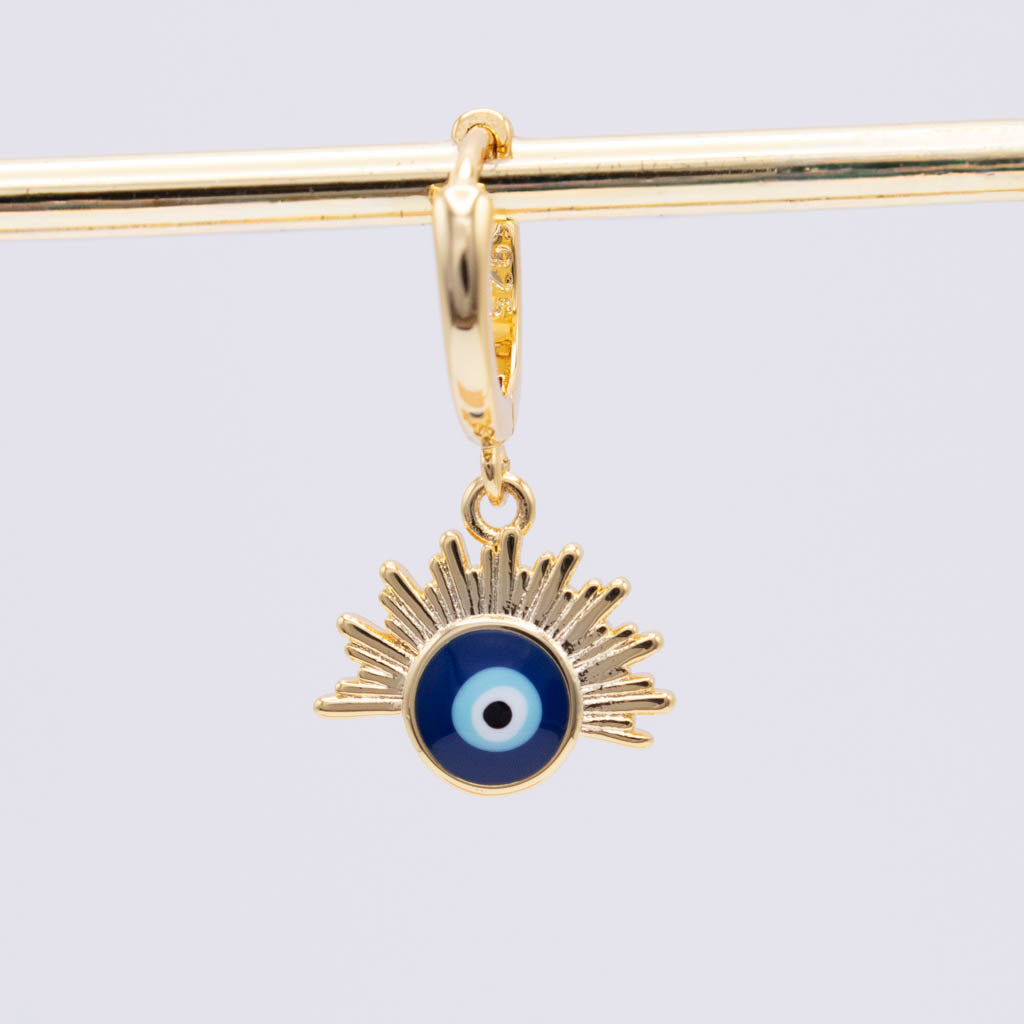 A gold charm featuring an evil eye pendant with a blue, white, and black center, suspended from a gold bar against a light gray background.