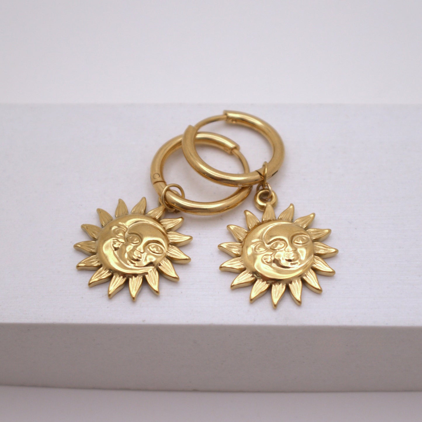 Gold hoop earrings with sun-shaped charms on a white background