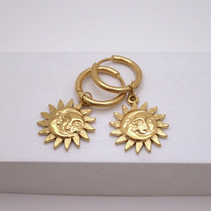 Gold hoop earrings with sun-shaped charms on a white background