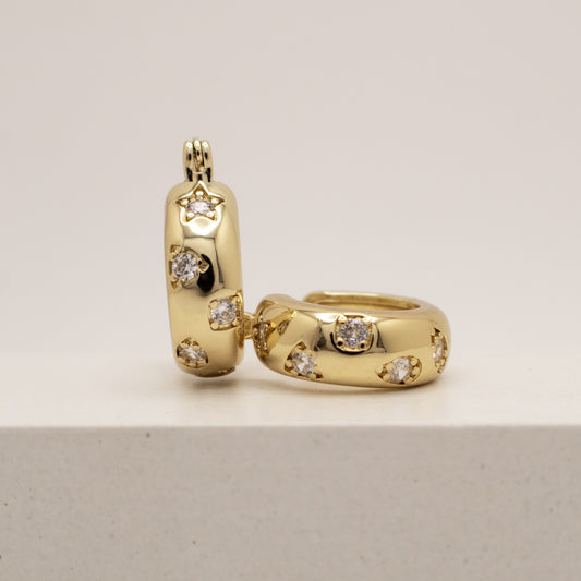 Gold hoop earrings with embedded diamonds on a light gray background