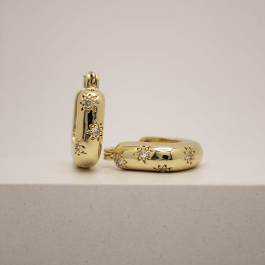 Gold hoop earrings with embedded diamonds on a light gray background