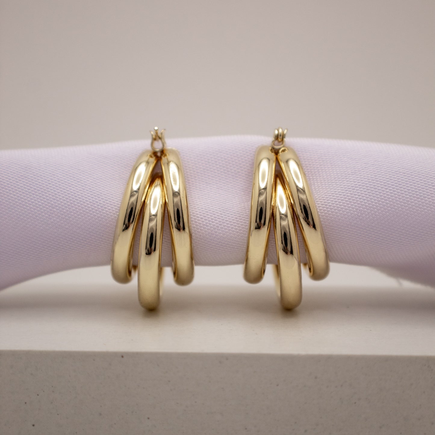 Gold hoop earrings on a light purple cushion with a neutral background