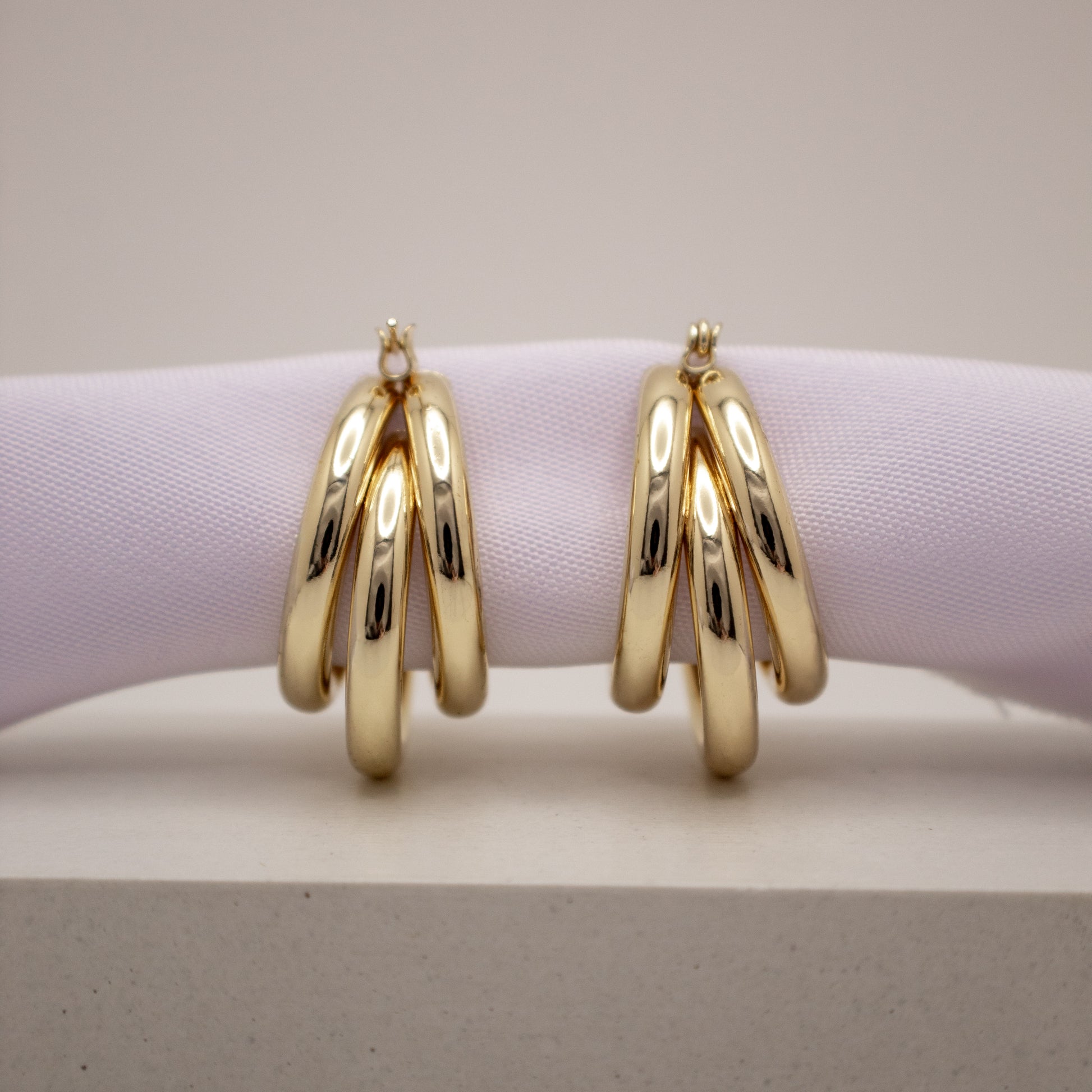 Gold hoop earrings on a light purple cushion with a neutral background