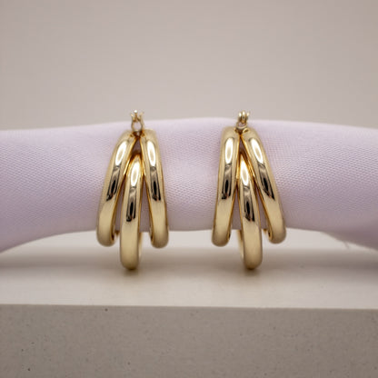 Gold hoop earrings on a light purple cushion with a neutral background