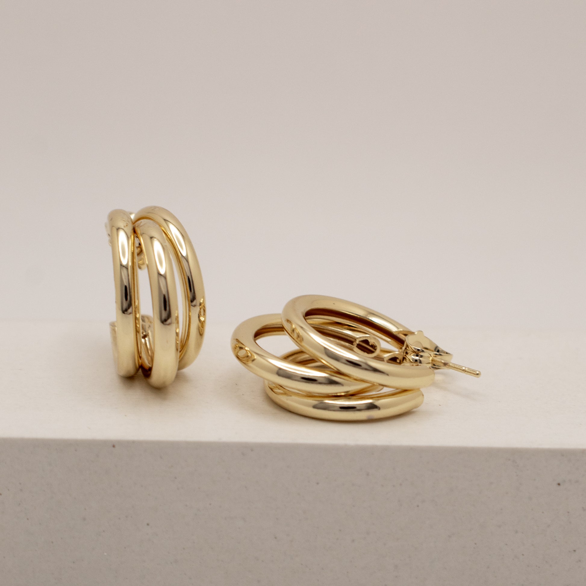Gold hoop earrings on a light gray surface with a neutral background