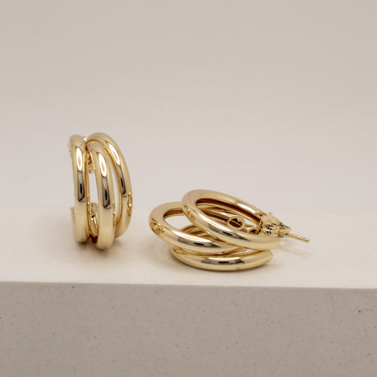 Gold hoop earrings on a light gray surface with a neutral background