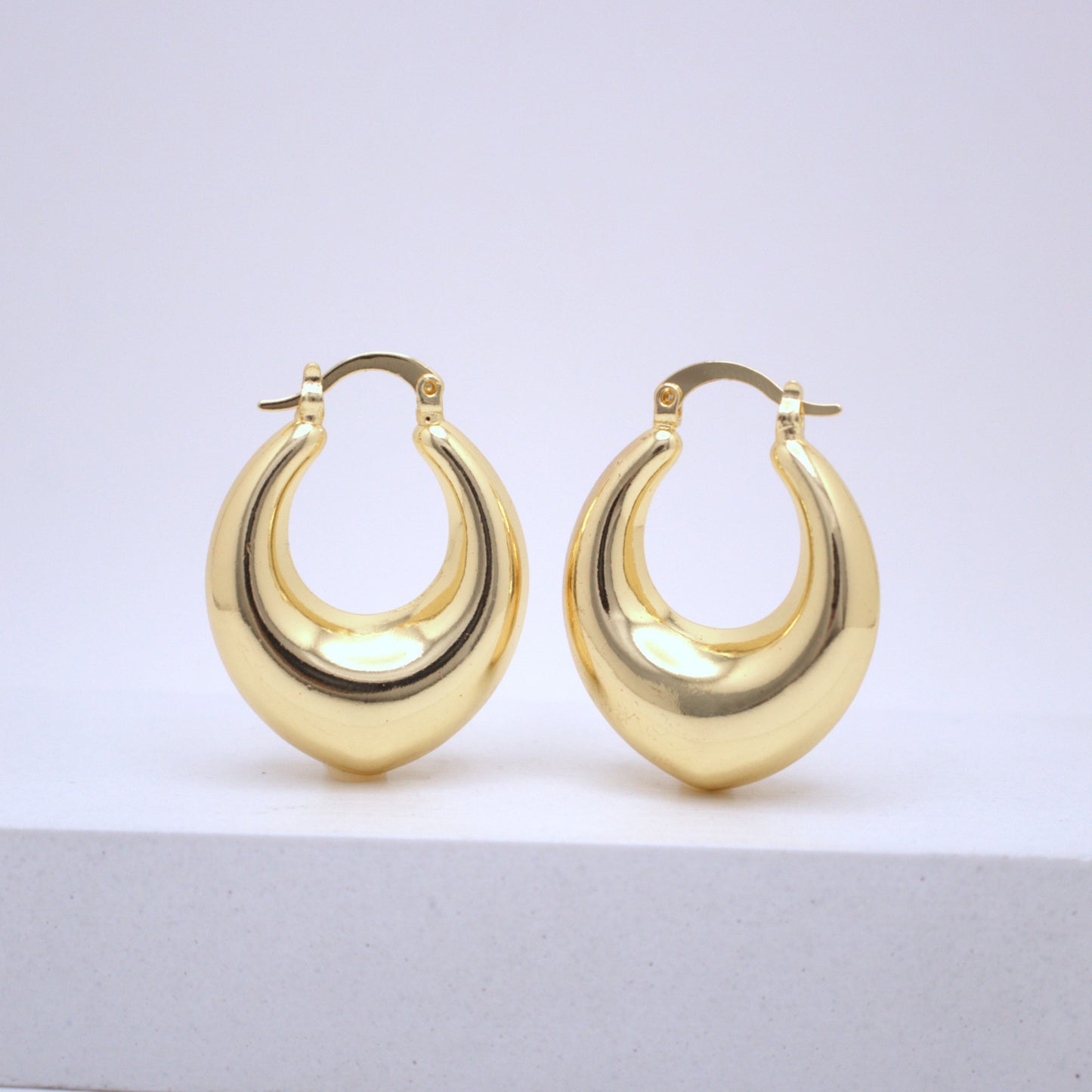 Pair of gold hoop earrings on a light gray surface with a white background