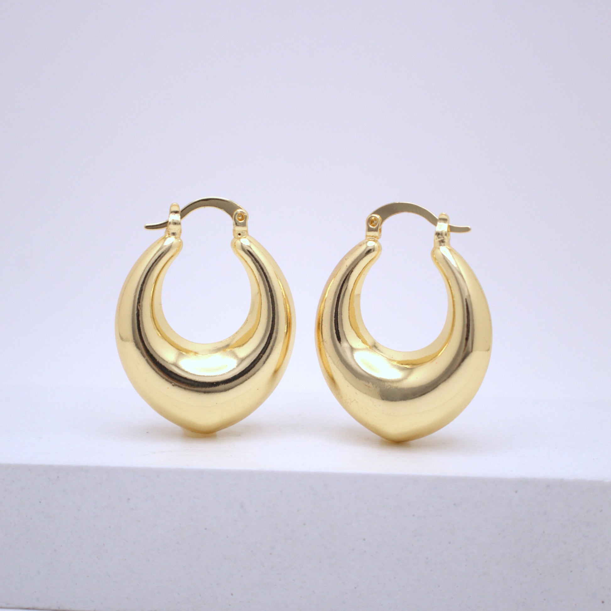 Pair of gold hoop earrings on a light gray surface with a white background