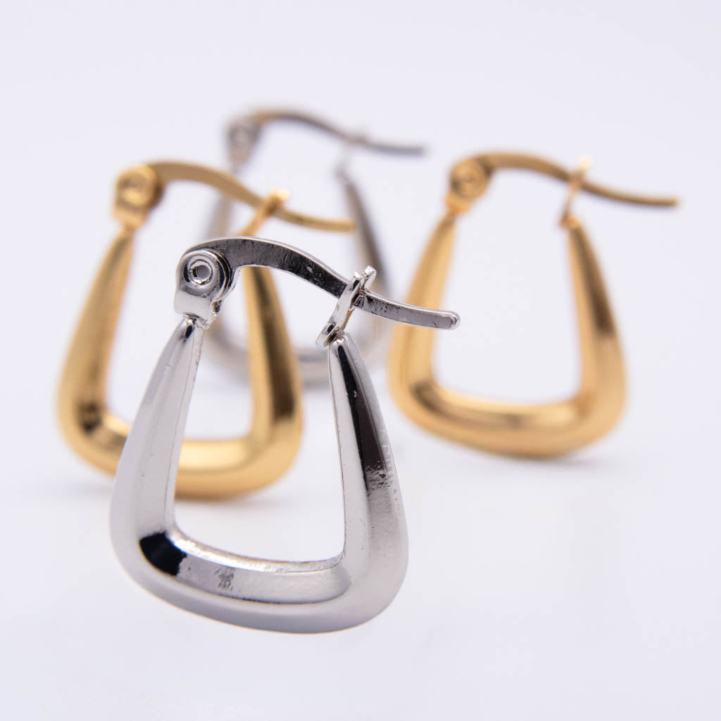 Three modern open hoop earrings with a triangular shape, shown in polished silver and yellow gold finishes on a clean white background.