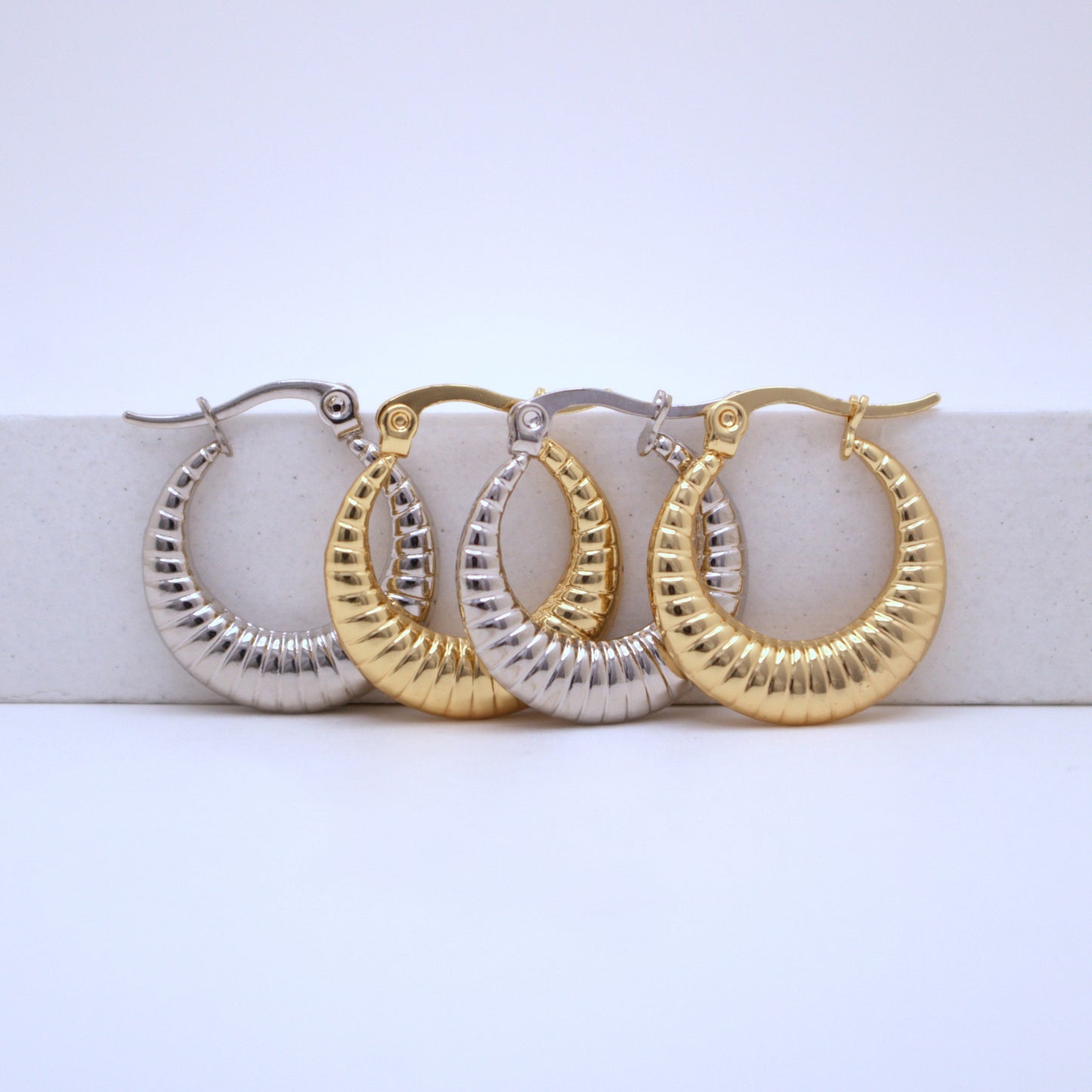 Pair of gold and silver hoop earrings on a white surface with a light blue background