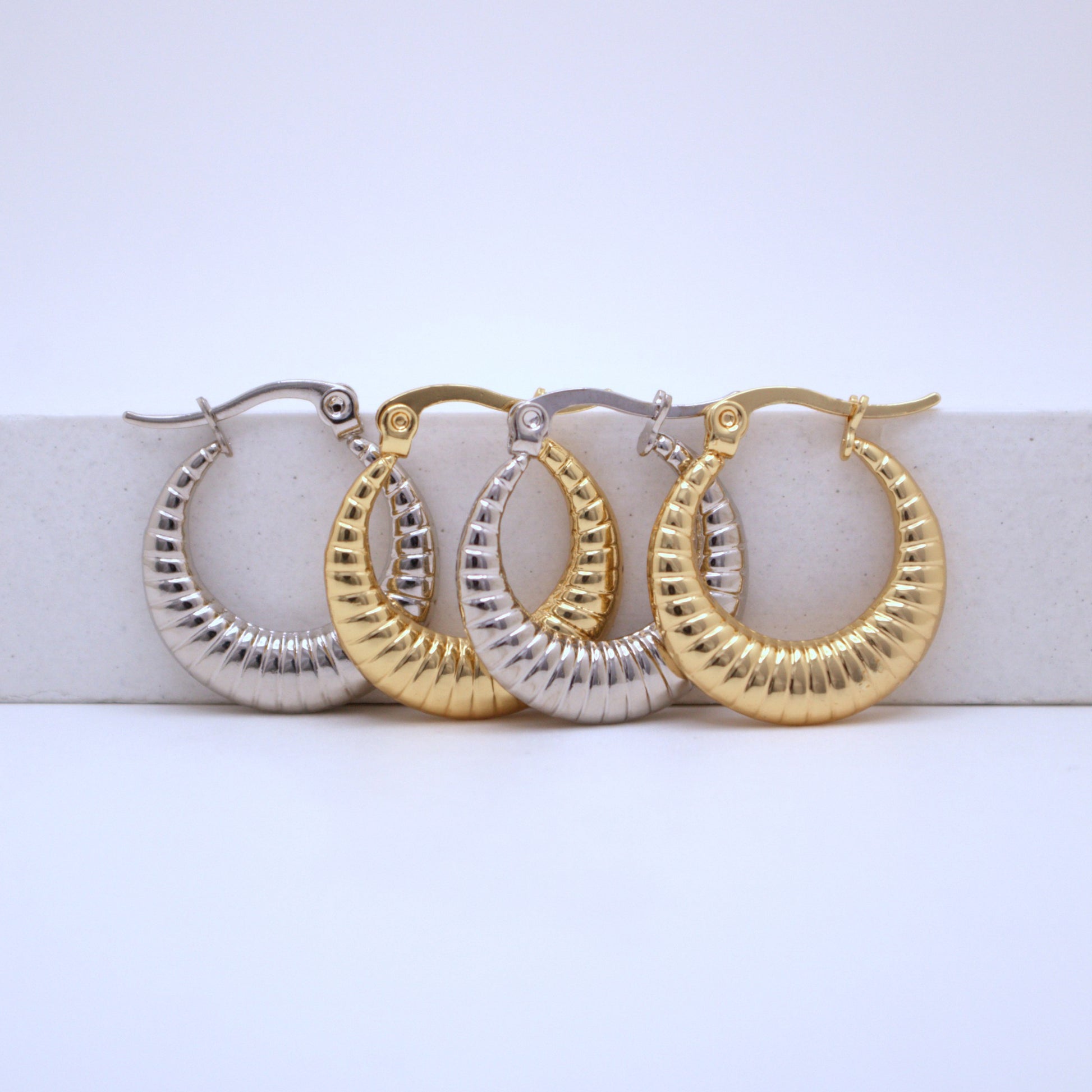 Pair of gold and silver hoop earrings on a white surface with a light blue background