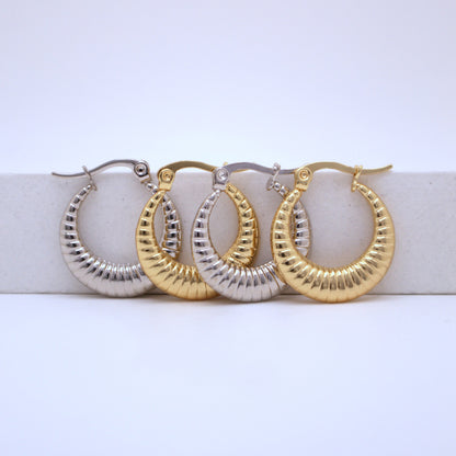 Pair of gold and silver hoop earrings on a white surface with a light blue background