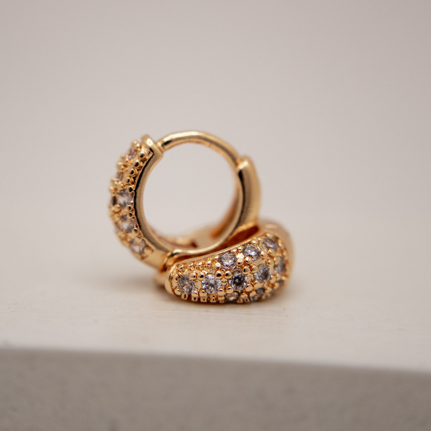 Gold hoop earring with embedded stones on a neutral background