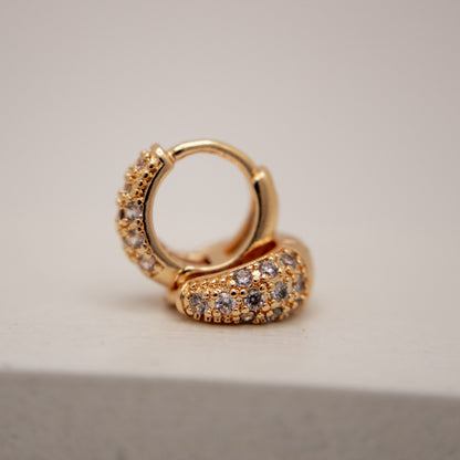 Gold hoop earring with embedded stones on a neutral background