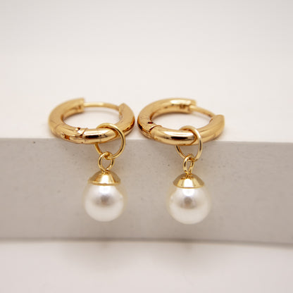 Gold hoop earrings with pearl drops on a light background