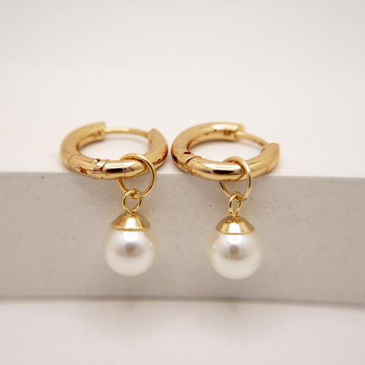 Gold hoop earrings with pearl drops on a light background