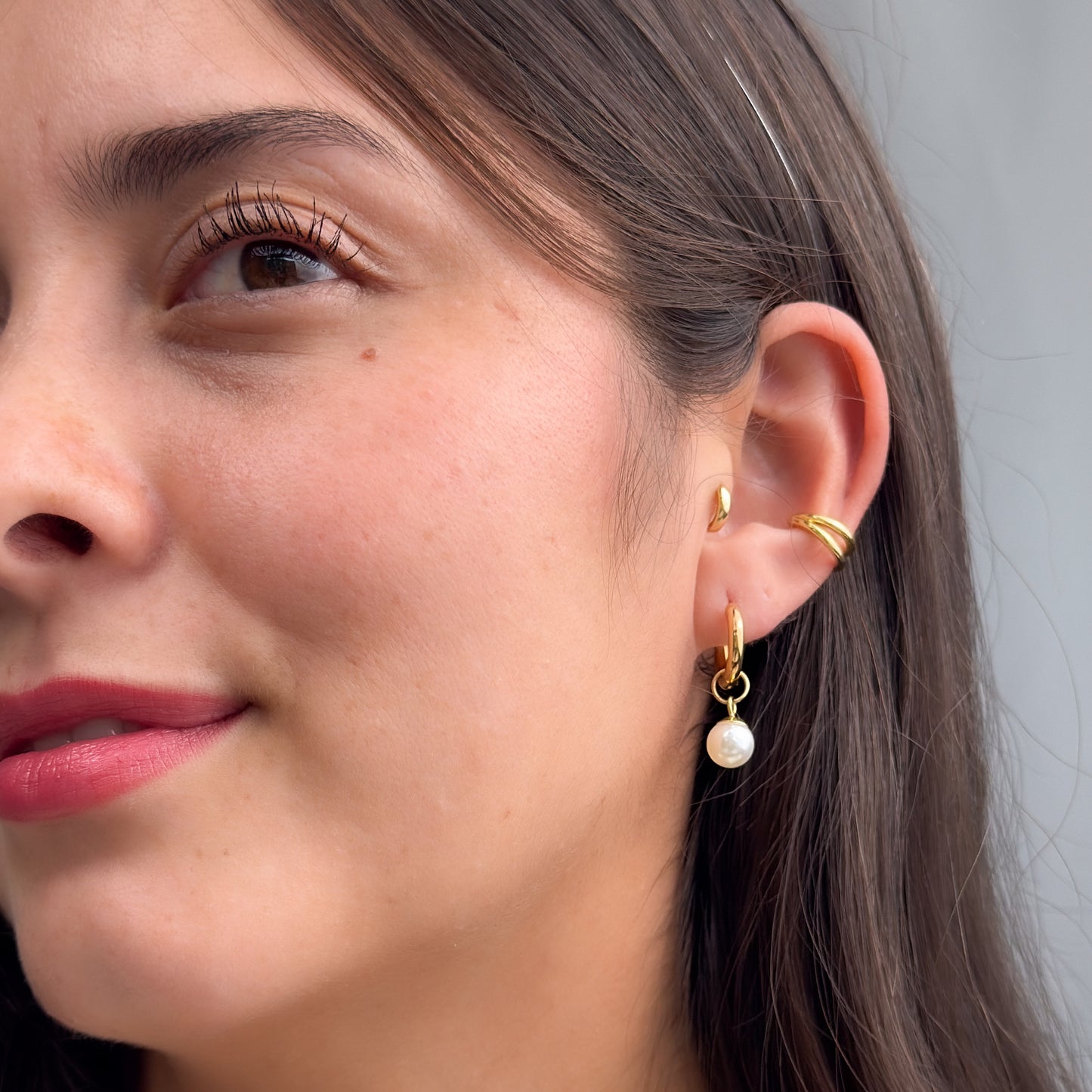 Close-up of a woman's ear wearing gold earrings and a ring.