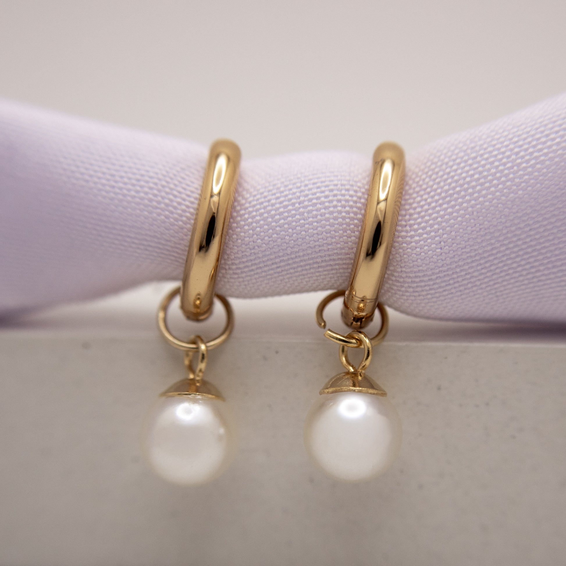 Gold hoop earrings with pearl drops on a light purple cushion.