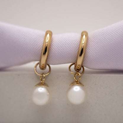 Gold hoop earrings with pearl drops on a light purple cushion.