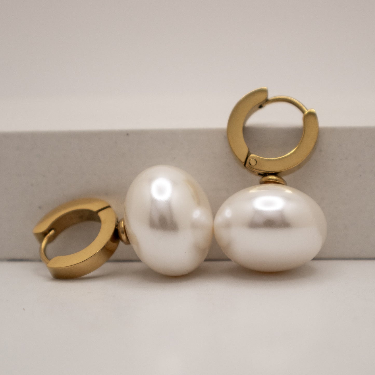 Gold hoop earrings with large white pearls on a light background