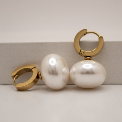Gold hoop earrings with large white pearls on a light background