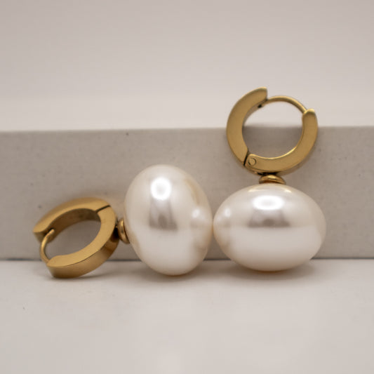 Gold hoop earrings with large white pearls on a light background