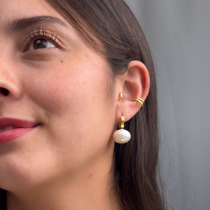 Close-up of a woman wearing gold hoop earrings and a pearl earring.