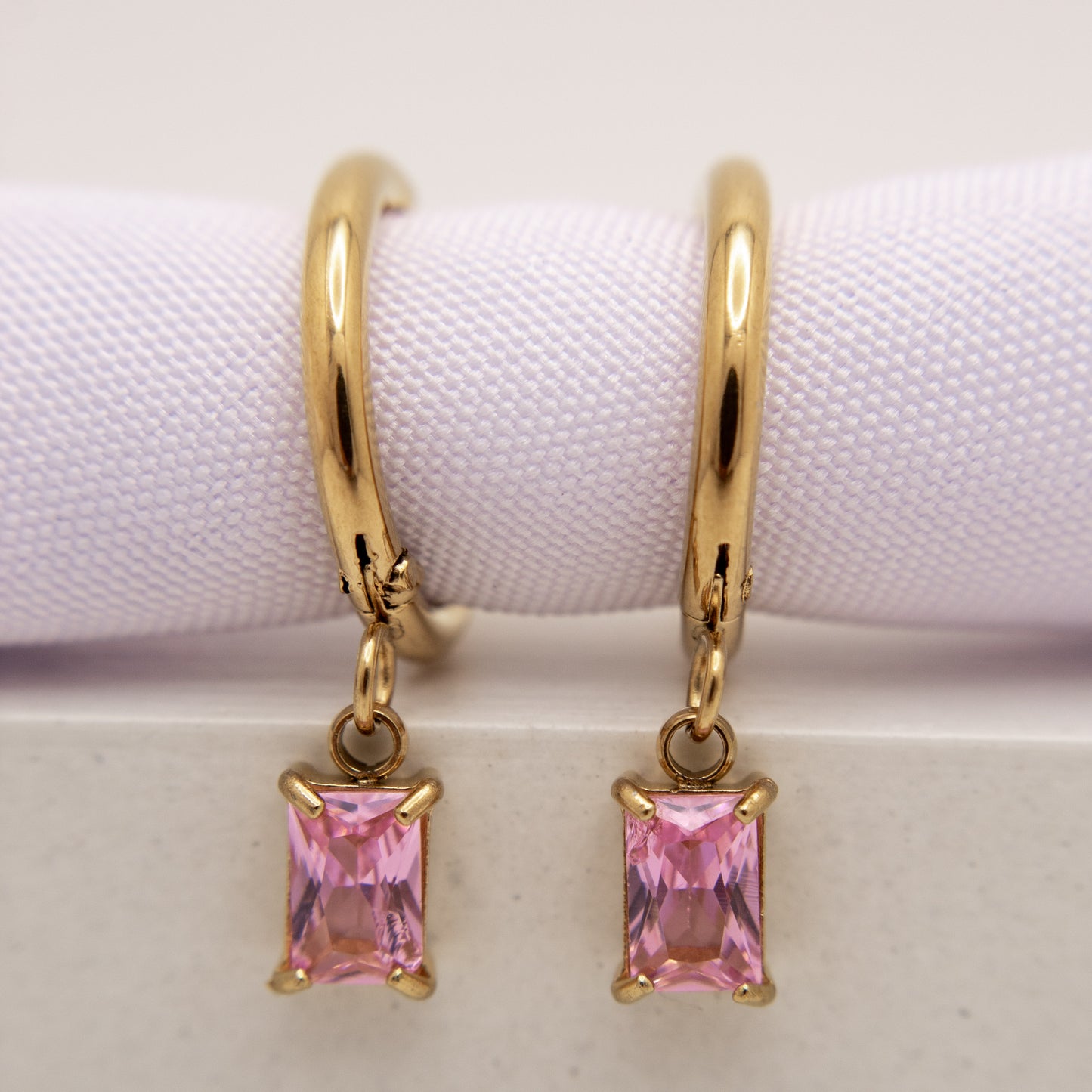 Gold hoop earrings with pink gemstones on a white background