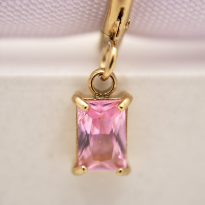 Gold pendant with a pink gemstone on a light fabric background