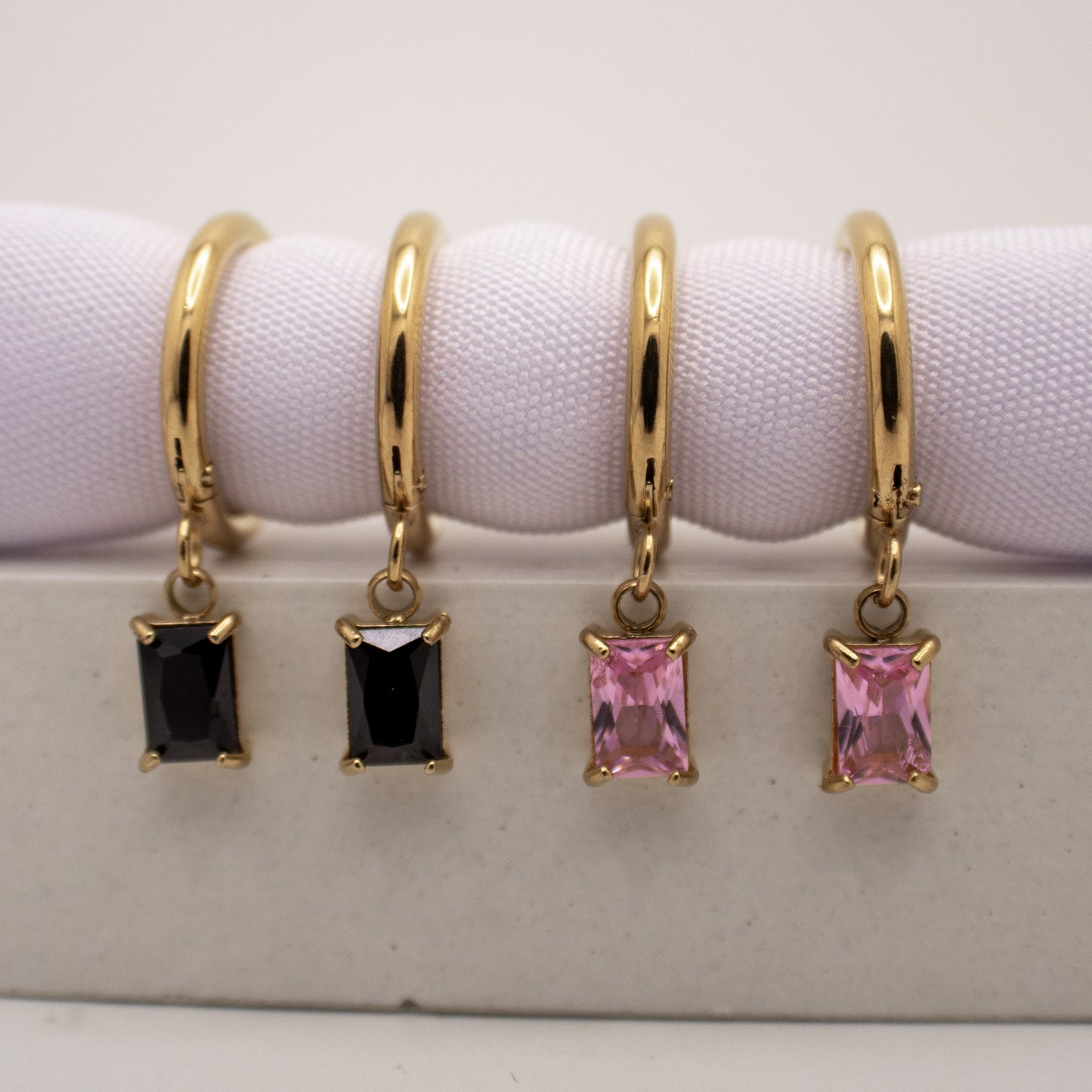 Gold hoop earrings with black and pink gemstones on a white background