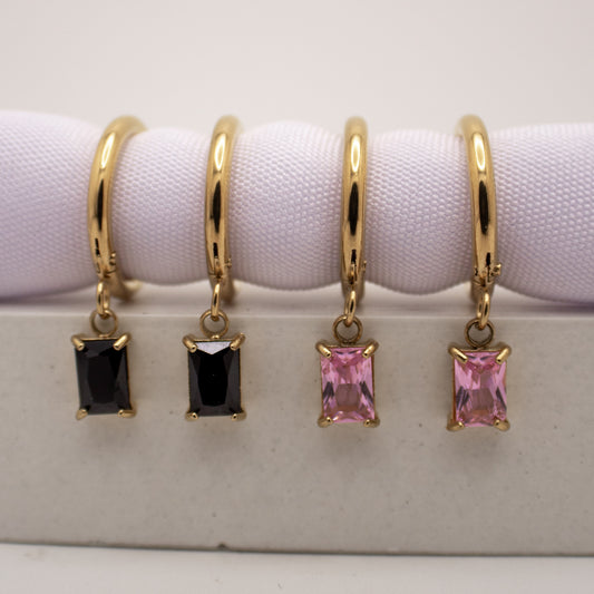 Gold hoop earrings with black and pink gemstones on a white background
