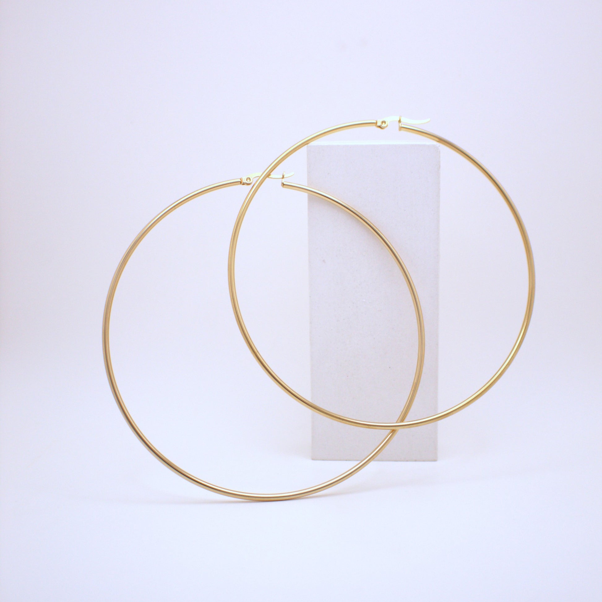 Gold hoop earrings on a white cylindrical stand against a light purple background