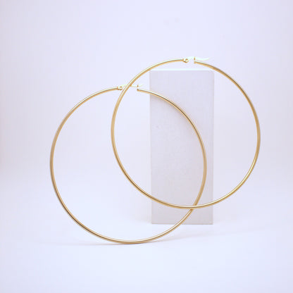 Gold hoop earrings on a white cylindrical stand against a light purple background