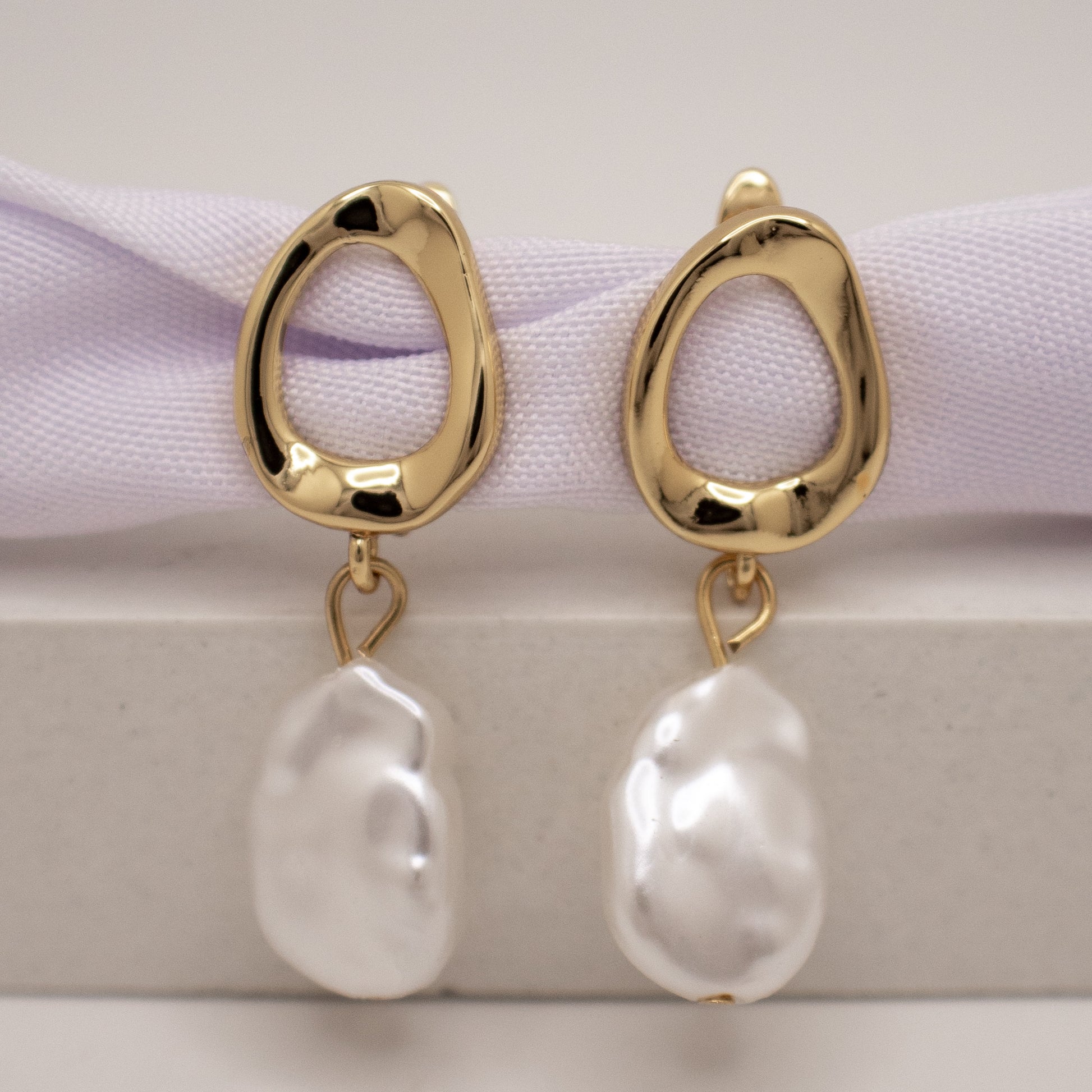 Gold earrings with white pearls on a light background