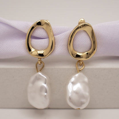 Gold earrings with white pearls on a light background