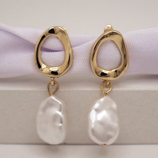 Gold earrings with white pearls on a light background