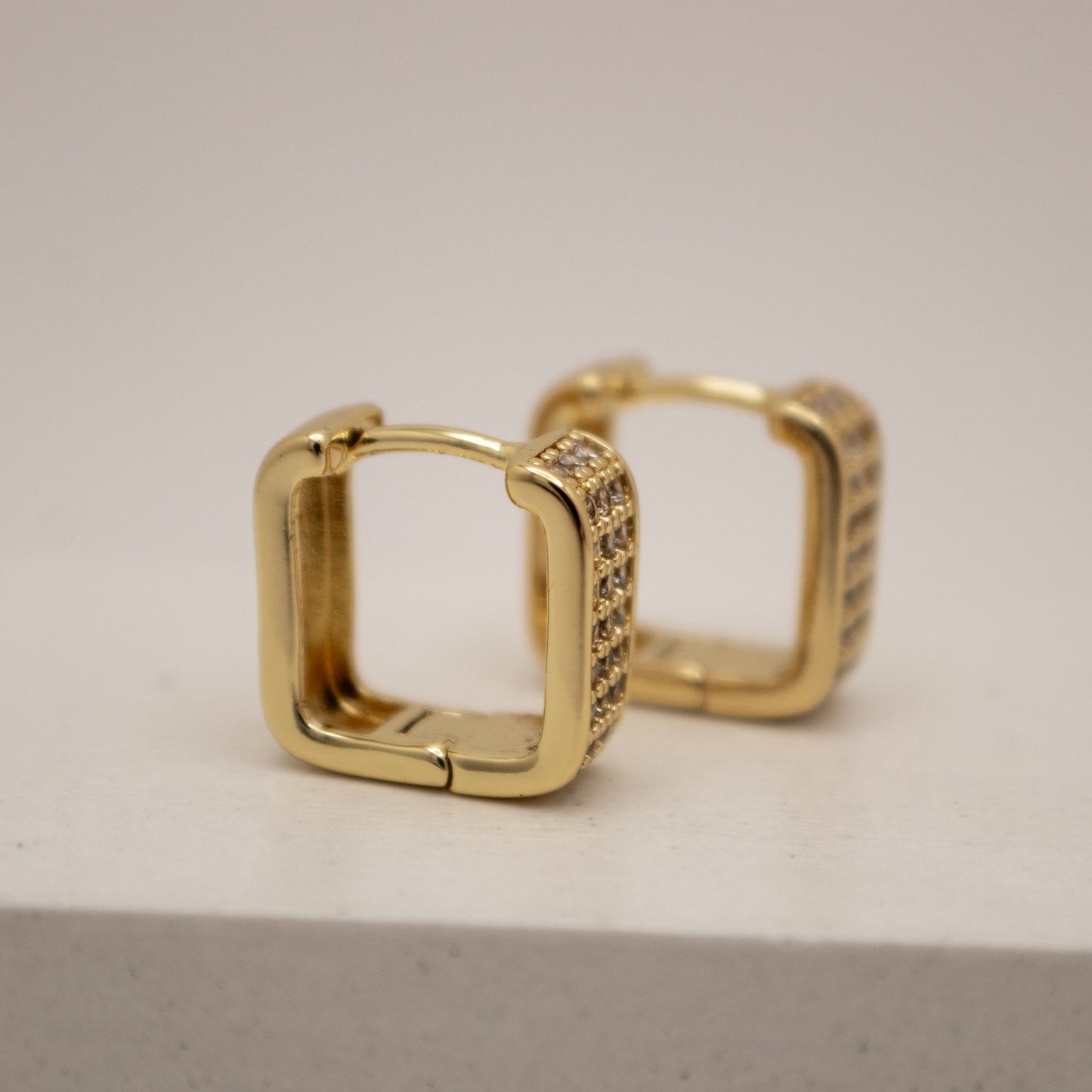 Gold hoop earrings with embedded stones on a light gray background