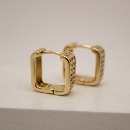 Gold hoop earrings with embedded stones on a light gray background