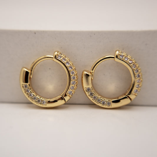 Gold hoop earrings with gemstones on a light beige background