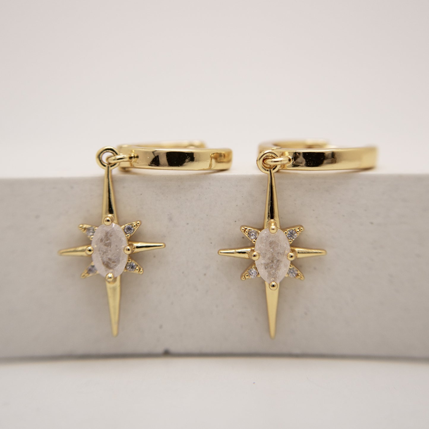 Gold hoop earrings with star-shaped drops on a light gray background