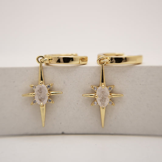 Gold hoop earrings with star-shaped drops on a light gray background