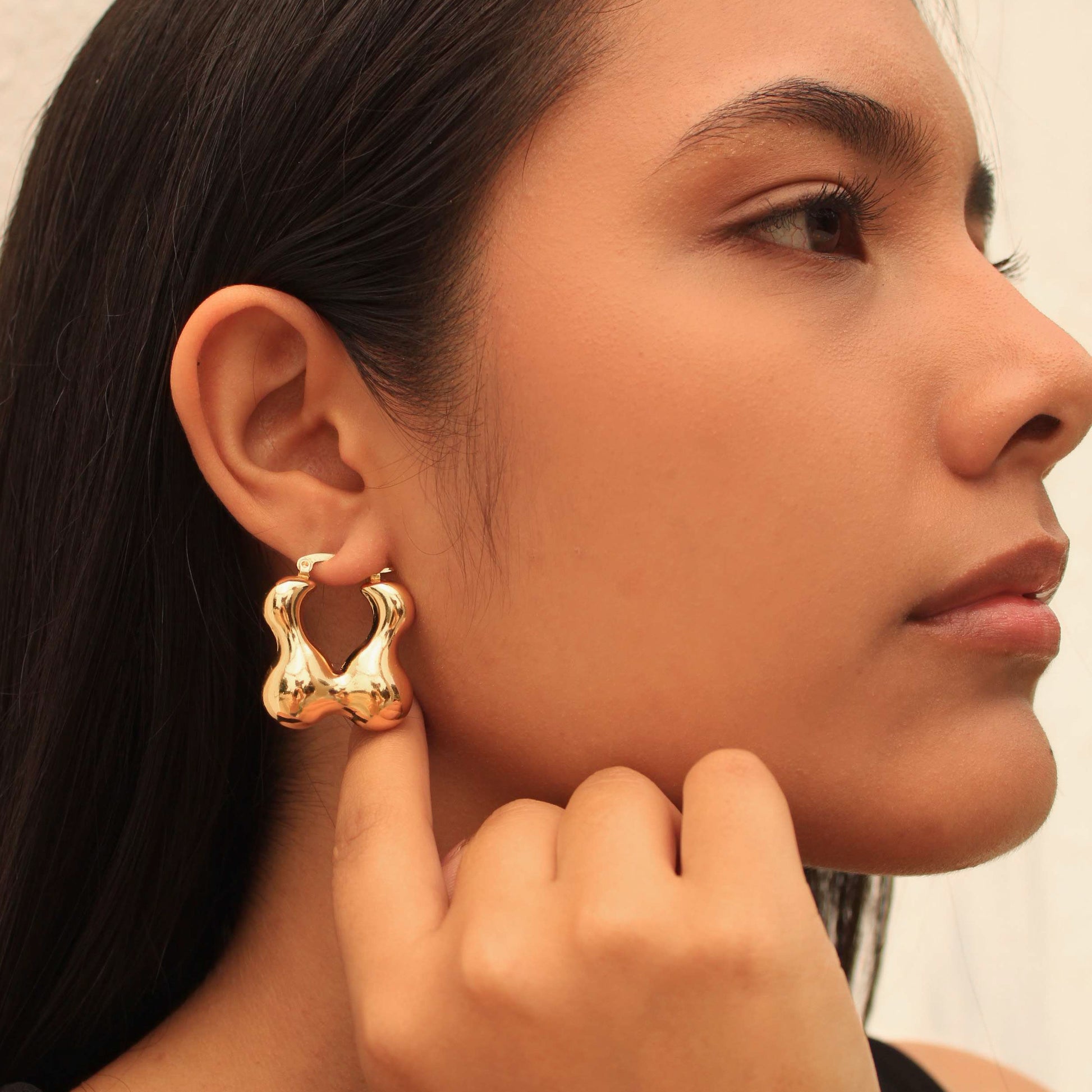 Close-up of a woman wearing gold hoop earrings with a neutral background
