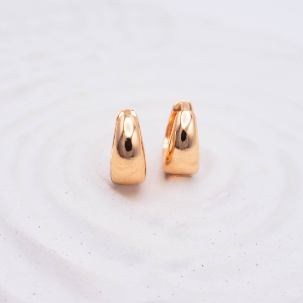 A pair of small polished rose gold hoop earrings standing upright on a light textured white surface.