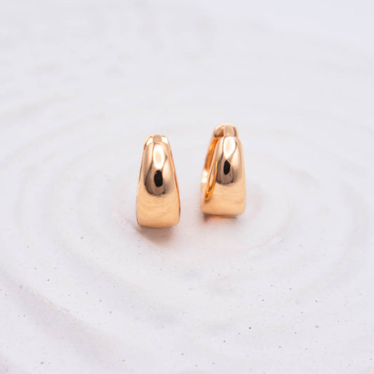 A pair of small polished rose gold hoop earrings standing upright on a light textured white surface.
